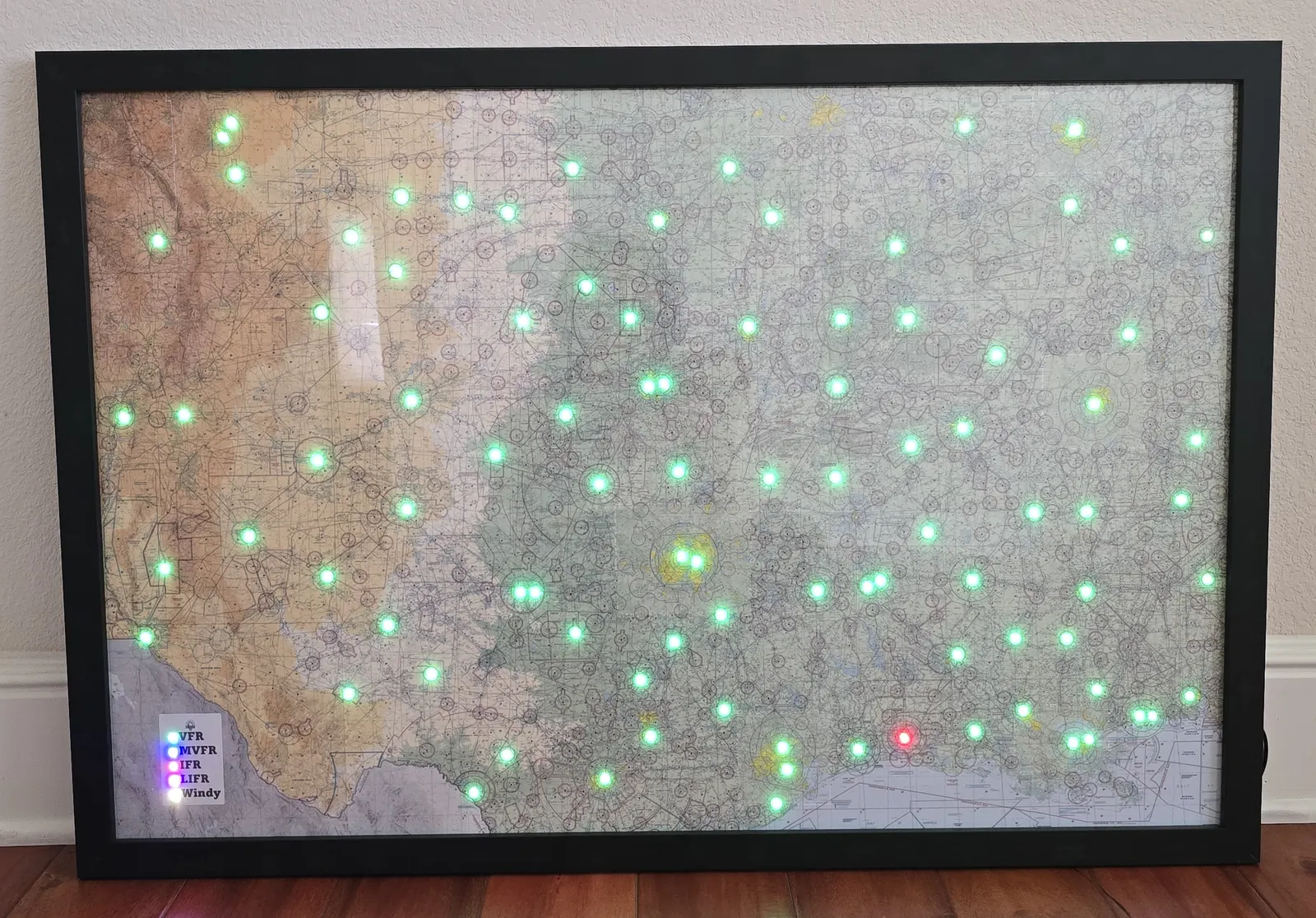 A large framed sectional map with dozens of green lights, leaning on a wall